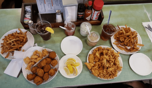 A table spread with fried chicken, fries, lemon wedges, and drinks in a casual dining setting.