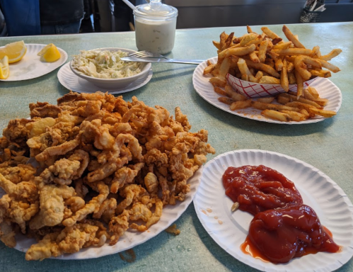 A table with plates of fried seafood, French fries, coleslaw, lemon wedges, and ketchup.
