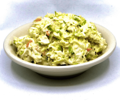 A bowl of creamy coleslaw with shredded cabbage and carrots, garnished with green herbs.