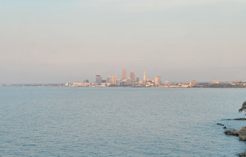 View of a city skyline across a calm lake, with buildings reflecting soft light in the distance.