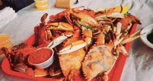 A large platter of cooked crabs with a bowl of seasoning on the side, served on a table.
