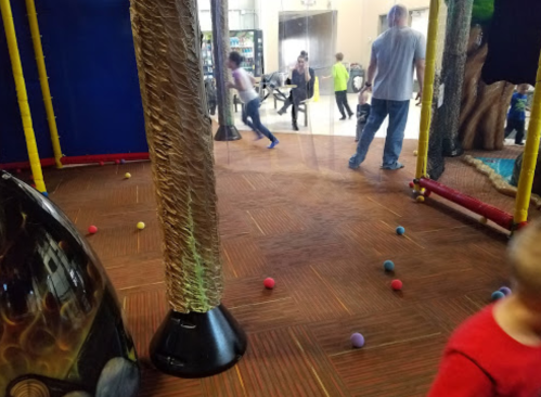 Children playing in a colorful indoor play area with various textures and soft balls scattered on the floor.