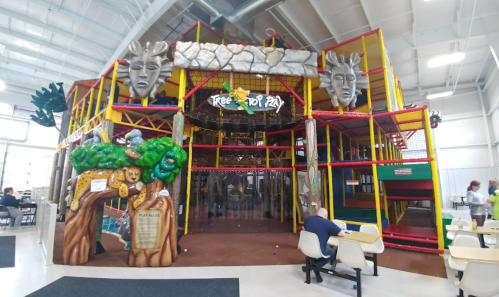 Colorful indoor play structure with jungle theme, featuring large animal sculptures and climbing areas.