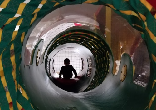A child sits inside a colorful play tunnel, looking out towards a bright opening.