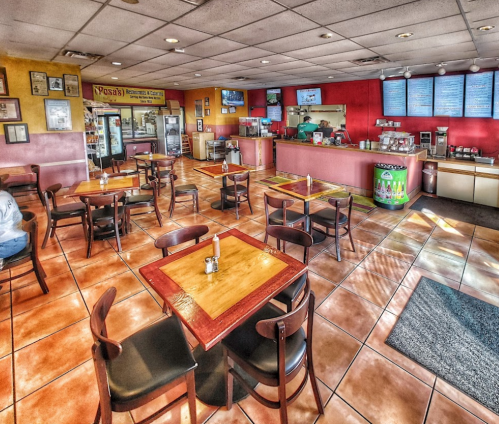 Interior of a casual restaurant with wooden tables, chairs, and colorful walls, featuring a counter and menu boards.