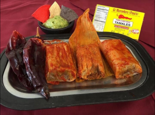 A platter of three red tamales with guacamole and colorful tortilla chips, accompanied by dried chiles.