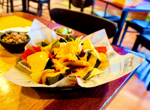 A plate of colorful nachos topped with melted cheese, served in a restaurant setting.