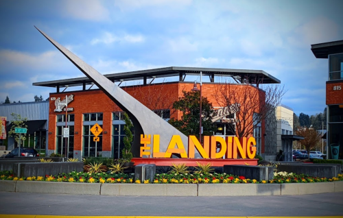 A large sign reading "The Landing" in front of a modern building, surrounded by colorful flowers and greenery.