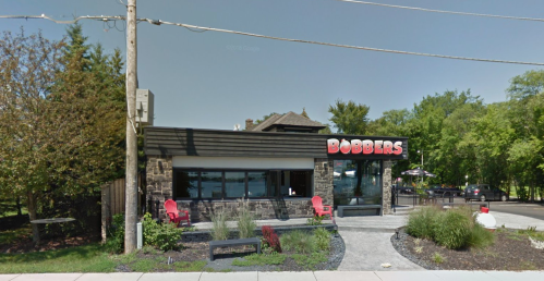 Exterior view of Bobbers restaurant, featuring a modern design, outdoor seating, and landscaping on a sunny day.