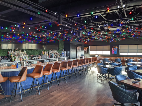 A modern bar interior with colorful string lights, a long bar counter, and stylish seating arrangements.