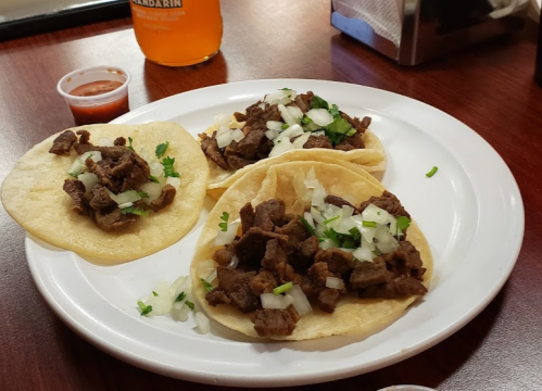 Three tacos filled with seasoned beef, topped with onions and cilantro, served with a side of salsa.