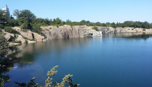 A serene lake surrounded by rocky cliffs and trees under a clear blue sky.