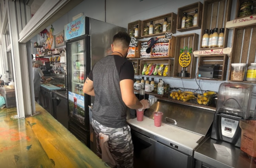 A person prepares smoothies at a colorful counter filled with ingredients and decorations in a vibrant café.