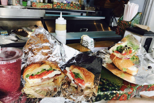 A variety of sandwiches wrapped in foil, with a smoothie on the side, set on a colorful table.