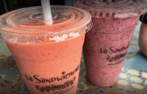 Two colorful smoothie cups with straws, one pink and one purple, from La Sandwicherie.