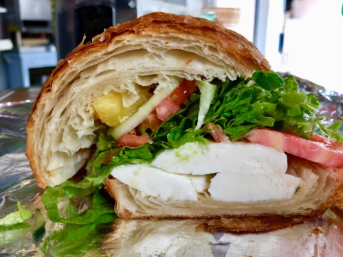 A cross-section of a croissant sandwich filled with lettuce, tomato, cheese, and pineapple.