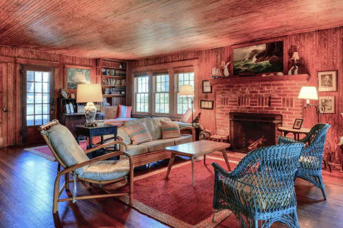 Cozy living room with wooden walls, a brick fireplace, comfortable seating, and warm lighting.
