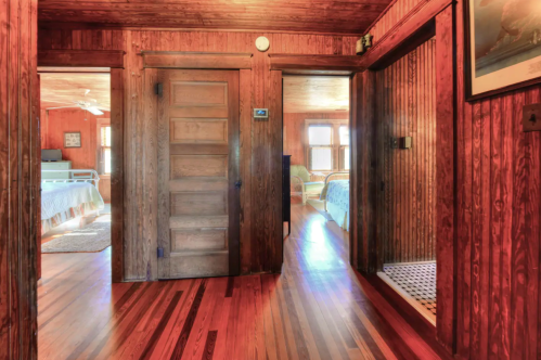 A warm wooden hallway with doors leading to rooms, featuring polished floors and natural light.