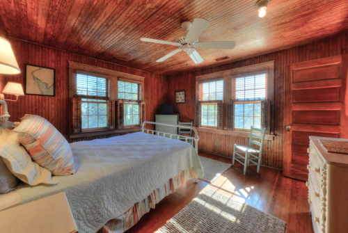 Cozy bedroom with wooden walls, a bed, a chair, and large windows letting in natural light.