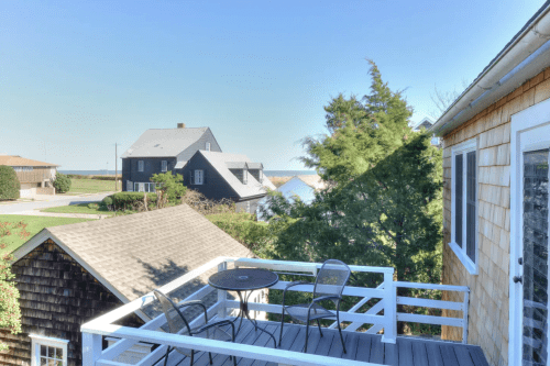 A view from a balcony overlooking houses and trees, with a clear blue sky in the background.