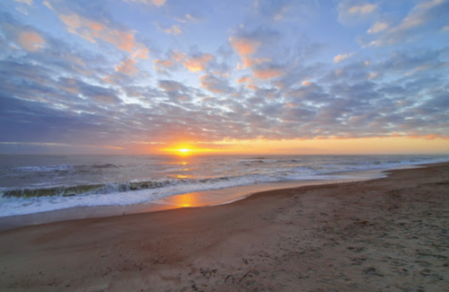 A serene beach at sunset, with gentle waves and a colorful sky filled with clouds.