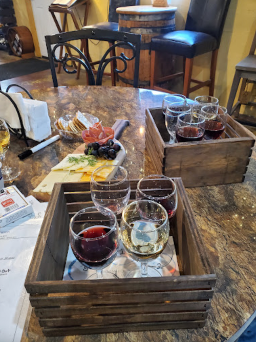 A wooden tray with wine glasses and a charcuterie board featuring cheese, meats, and fruits on a table.