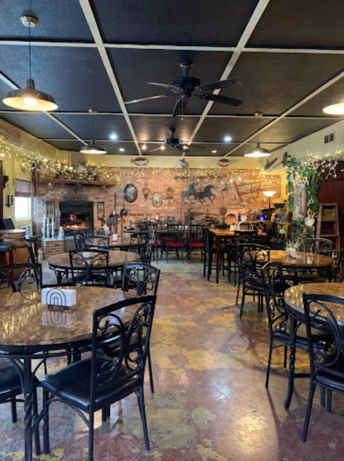 Cozy restaurant interior with brick walls, round tables, and rustic decor, featuring a fireplace and warm lighting.