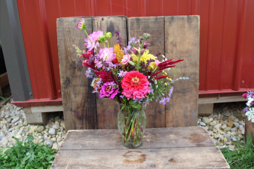 A vibrant bouquet of mixed flowers in a glass vase, set against a rustic wooden backdrop.