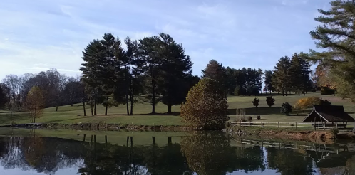 A serene landscape featuring a calm lake, trees, and rolling hills under a clear blue sky.