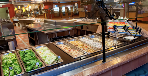 A salad bar with various fresh ingredients, including greens, pasta, and toppings, in a restaurant setting.
