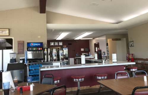 Interior of a diner featuring a counter with drink dispensers and red vinyl stools, tables, and a casual atmosphere.