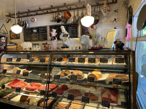 A display case filled with various meats, labeled with black tags, in a charming butcher shop setting.