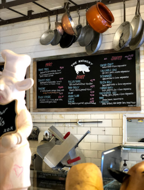 A chalkboard menu at a restaurant with various dishes listed, surrounded by hanging pots and kitchen equipment.