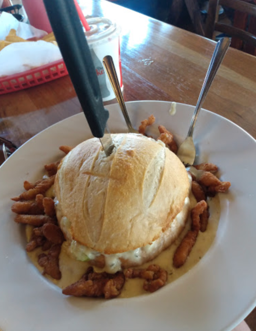 A large bread bowl filled with creamy sauce and topped with crispy fried onions, served on a plate with utensils.