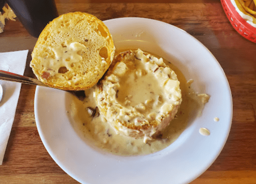 A bowl of creamy soup served in a bread bowl, with a top piece of the bread resting beside it.