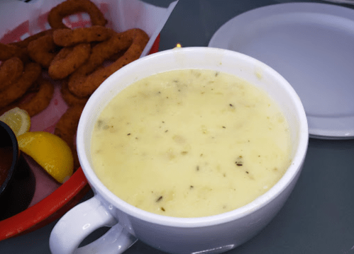 A bowl of creamy soup with herbs, accompanied by a plate of golden-brown onion rings and a lemon wedge.