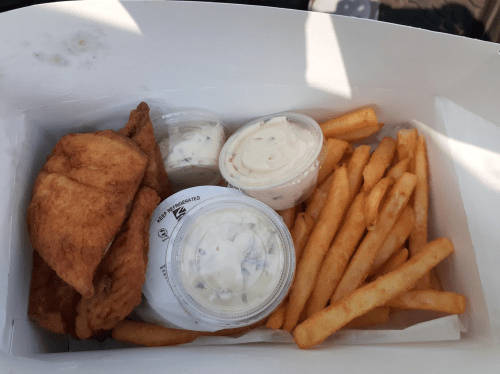 A takeout box containing fried fish, two cups of sauce, and a serving of French fries.