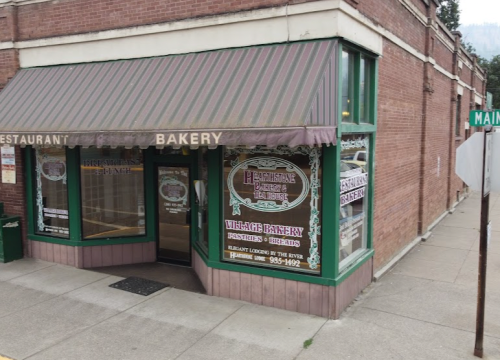 A corner bakery with a green awning and large windows, featuring signs for pastries and a restaurant.