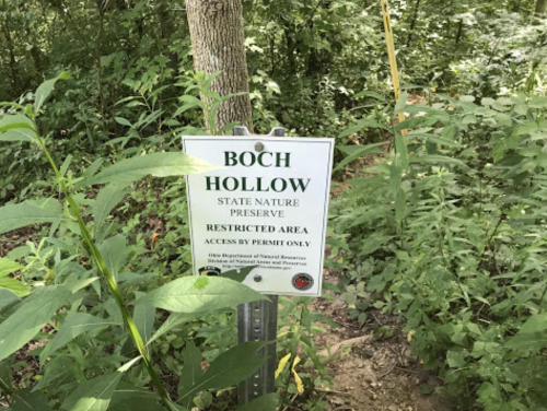 Sign for Boch Hollow State Nature Preserve, indicating a restricted area accessible by permit only, surrounded by greenery.