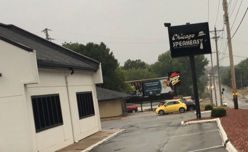 A rainy street scene featuring a building labeled "Chicago Speakeasy" and a yellow car parked nearby.