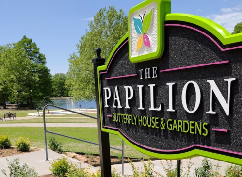 Sign for "The Papilion Butterfly House & Gardens" with a scenic view of a lake and greenery in the background.