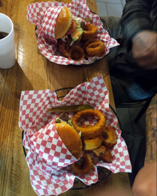 Two baskets with burgers and onion rings, served on red and white checkered paper, on a wooden table.