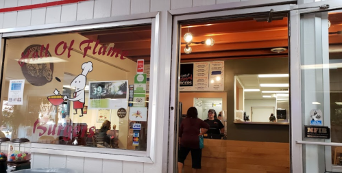 A restaurant entrance with a sign reading "Hall of Flame Burgers" and people inside. Brightly lit and welcoming atmosphere.