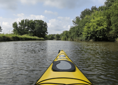 A yellow kayak on calm water, surrounded by lush green trees and a cloudy sky.
