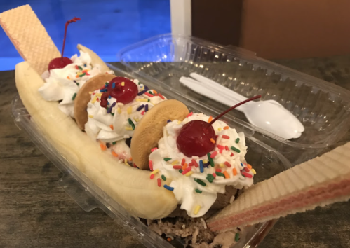 A banana split topped with whipped cream, cherries, sprinkles, and cookies, served in a clear container.