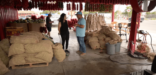 A market scene with people interacting among bags of produce and hanging decorations.