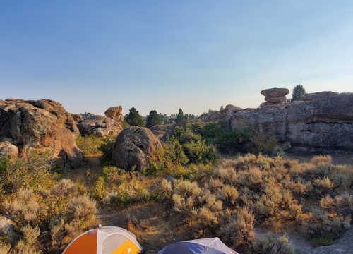A scenic view of rocky terrain and shrubs under a clear sky, with colorful tents in the foreground.