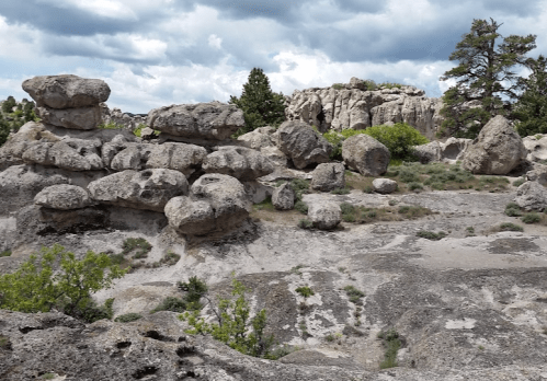 Rocky landscape with large boulders and sparse vegetation under a cloudy sky.