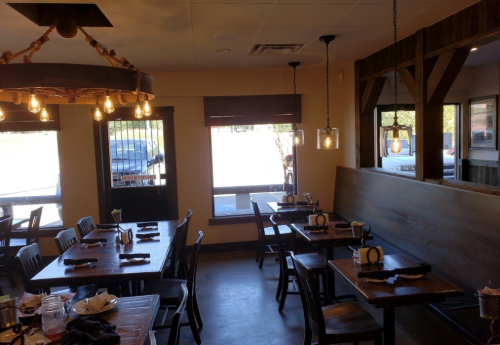 Cozy restaurant interior with wooden tables, chairs, and warm lighting, featuring large windows and a welcoming atmosphere.