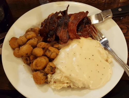 A plate of food featuring crispy bacon, fried okra, and creamy mashed potatoes with gravy.